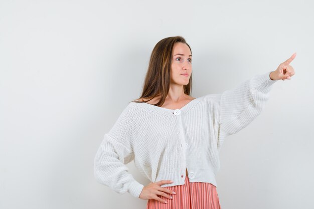 Junge Dame, die in Strickjacke und Rock weg zeigt, die zuversichtlich isoliert suchen