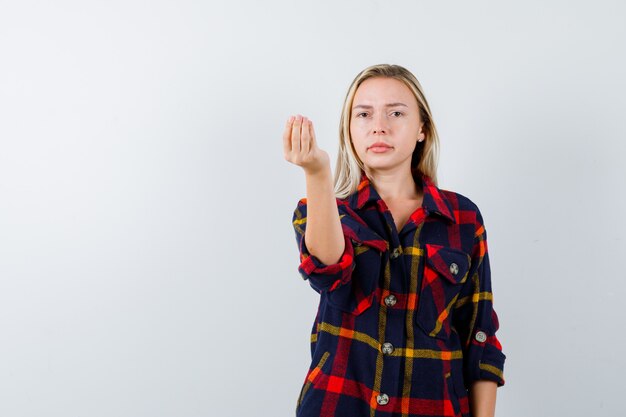 Junge Dame, die italienische Geste im karierten Hemd zeigt und entzückte Vorderansicht schaut.