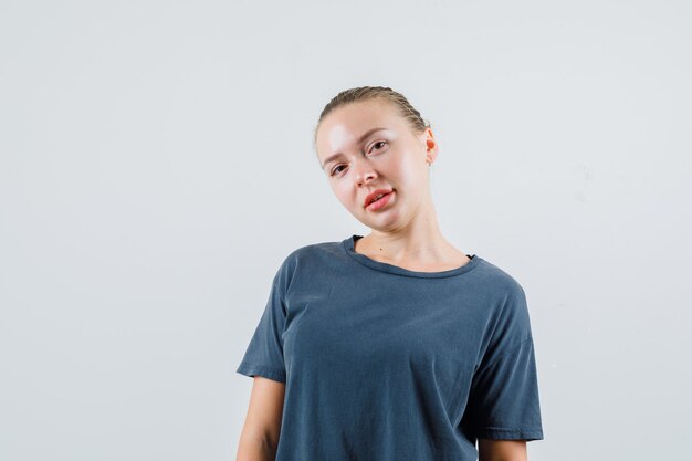 Junge Dame, die Kamera betrachtet und in der grauen T-Shirt-Vorderansicht lächelt.