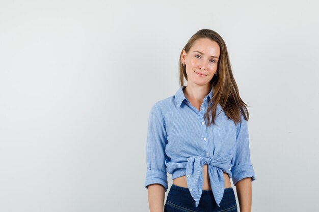 Junge Dame, die Kamera im blauen Hemd, in den Hosen betrachtet und fröhlich schaut.