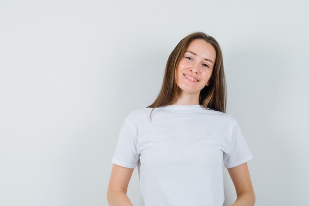 Junge Dame, die Kamera im weißen T-Shirt betrachtet und fröhlich schaut