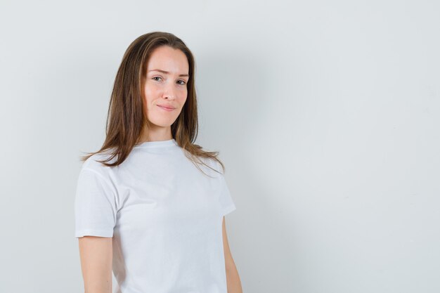 Junge Dame, die Kamera im weißen T-Shirt betrachtet und zuversichtlich schaut