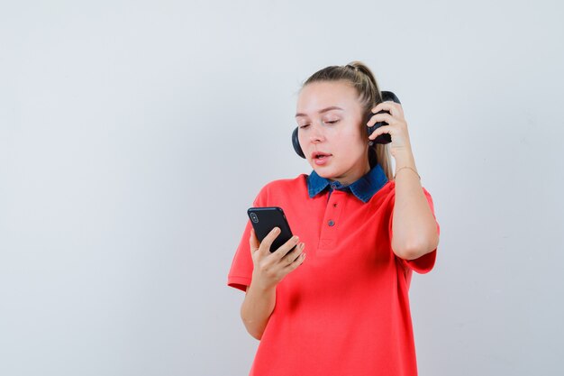 Junge Dame, die Kopfhörer abnimmt, mit Handy im T-Shirt