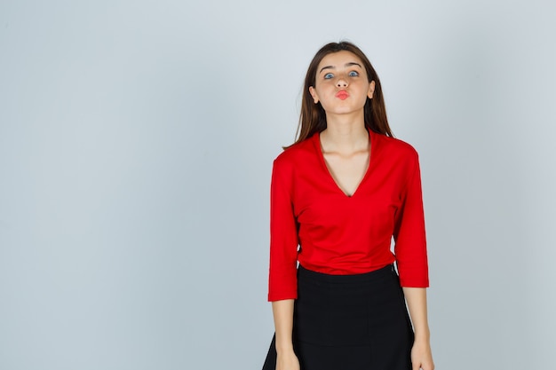 Junge Dame, die Kuss mit schmollenden Lippen in roter Bluse, Rock und hübsch aussehend sendet