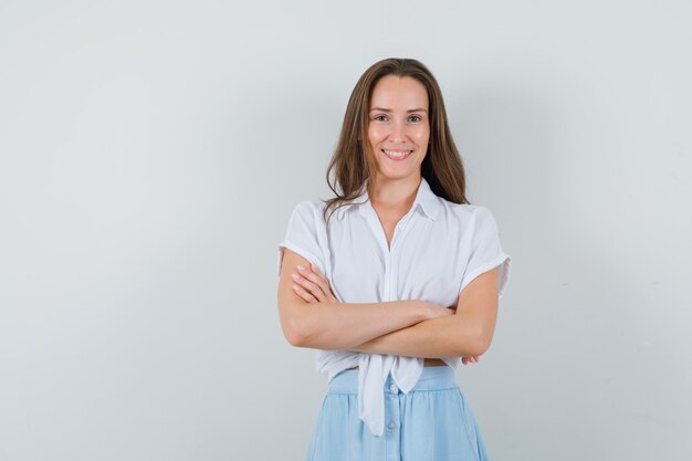 Junge Dame, die lächelt, während Arme in Bluse und Rock verschränkt hält und optimistisch aussieht