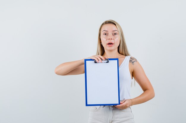 Junge Dame, die leere Zwischenablage in weißer Bluse hält und konzentriert schaut