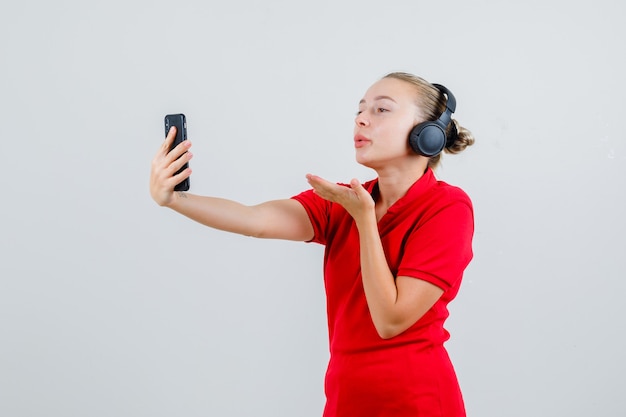 Junge Dame, die Luftkuss auf Videoanruf im roten T-Shirt und in den Kopfhörern sendet