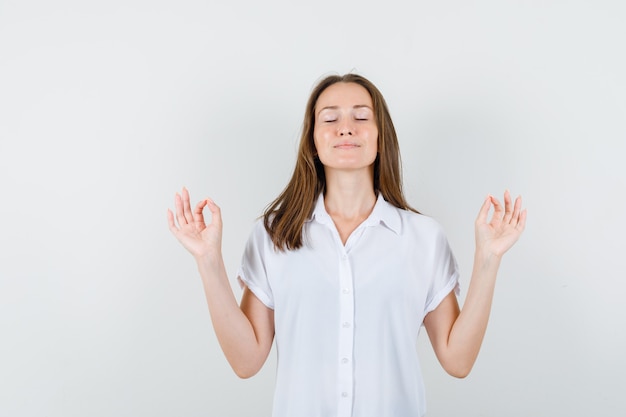 Junge Dame, die Meditation in der weißen Bluse tut und konzentriert schaut.