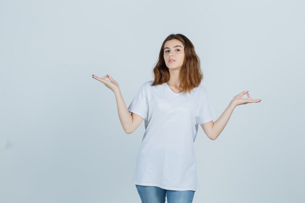 Junge Dame, die Meditationsgeste in T-Shirt, Jeans zeigt und friedlich, Vorderansicht schaut.