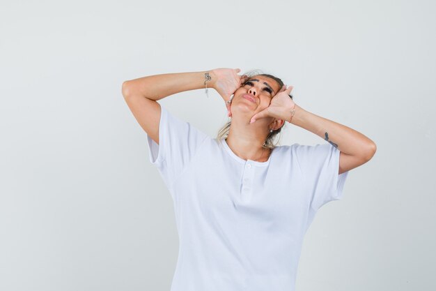 Junge Dame, die mit den Händen nahe den Augen im T-Shirt aufschaut