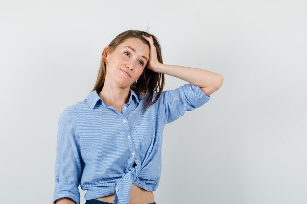 Junge Dame, die mit Hand im Haar im blauen Hemd, in der Hose wegschaut und verträumt schaut