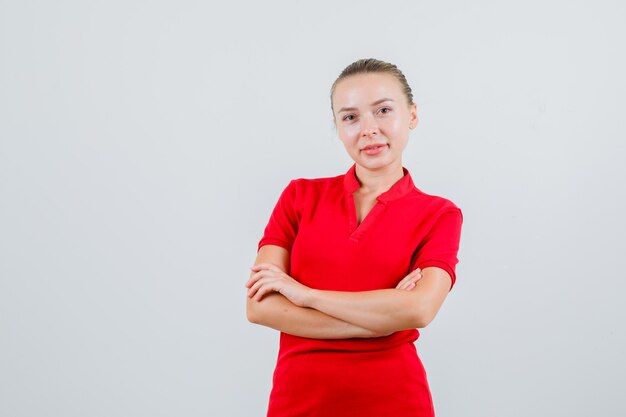 Junge Dame, die mit verschränkten Armen im roten T-Shirt steht und fröhlich schaut