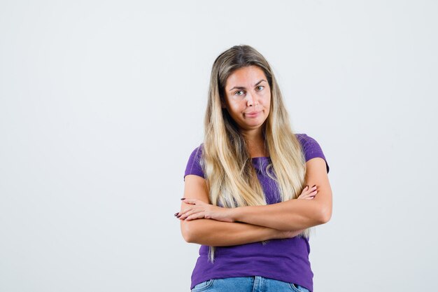 Junge Dame, die mit verschränkten Armen im T-Shirt, in den Jeans steht und selbstbewusst, Vorderansicht schaut.