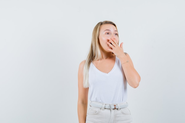 Junge Dame, die Mund mit Hand in weißer Bluse bedeckt und erstaunt schaut