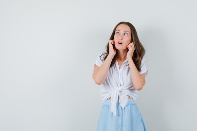 Junge Dame, die Ohren mit Fingern in Bluse, Rock verstopft und neugierig schaut