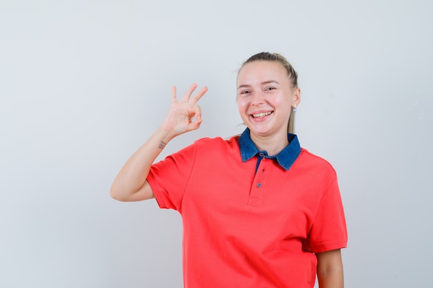 Junge Dame, die ok Geste im T-Shirt zeigt und fröhlich aussieht