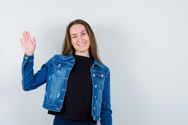 Junge Dame, die Palme in Bluse, Jacke zeigt und selbstbewusst aussieht, Vorderansicht.