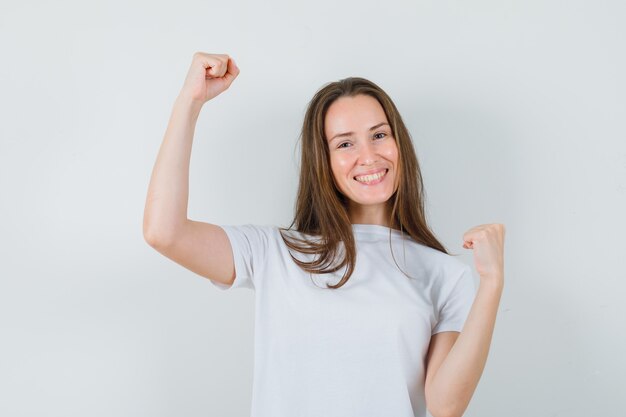 Junge Dame, die Siegergeste im weißen T-Shirt zeigt und glücklich schaut