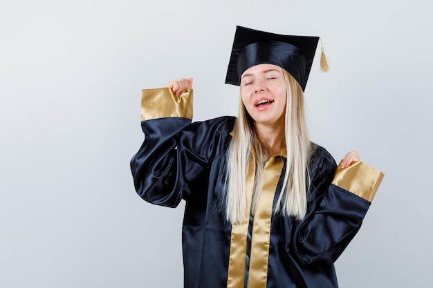 Junge Dame, die Siegergeste in akademischer Kleidung zeigt und glückselig aussieht.