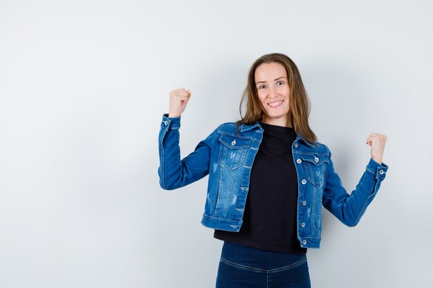 Junge Dame, die Siegergeste in Hemd, Jacke zeigt und glücklich aussieht. Vorderansicht.