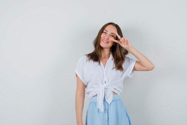 Junge Dame, die Siegesgeste in Bluse und Rock zeigt und fröhlich aussieht