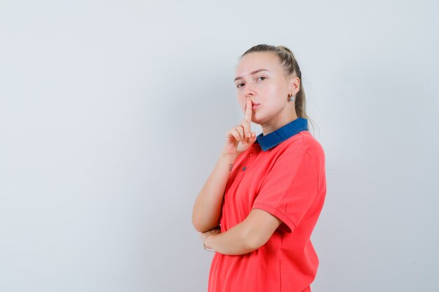 Junge Dame, die Stille Geste im T-Shirt zeigt und vorsichtig schaut