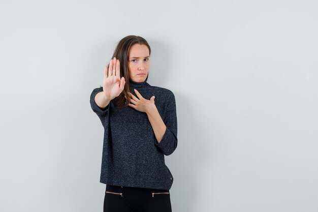 Junge Dame, die Stoppgeste im Freizeithemd zeigt und entschlossen schaut. Vorderansicht.