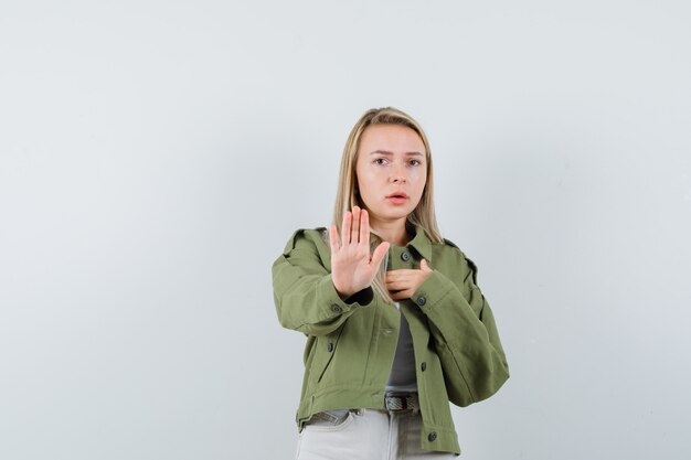 Kostenloses Foto junge dame, die stoppgeste in jacke, hose zeigt und ängstlich, vorderansicht schaut.