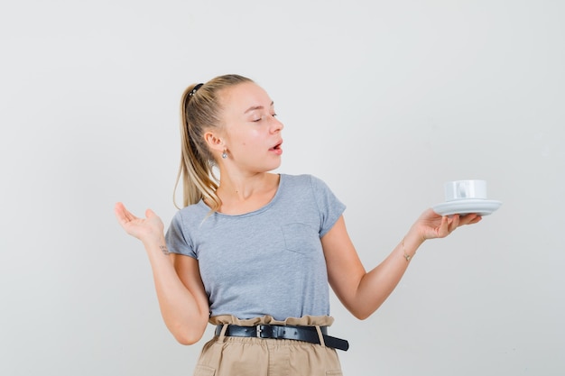 Junge Dame, die Tasse des Getränks im T-Shirt und in der Hose betrachtet und konzentriert schaut