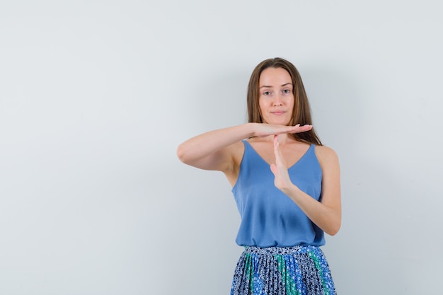 Junge Dame, die Trennungsgeste in der blauen Bluse, im Rock zeigt und ernst schaut. Vorderansicht.