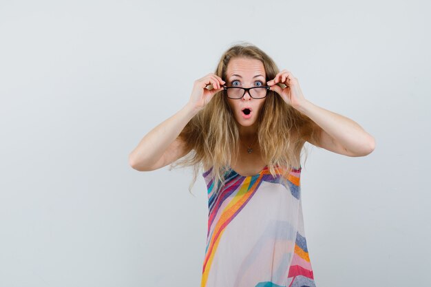 Junge Dame, die über Brille im Sommerkleid schaut und schockiert schaut