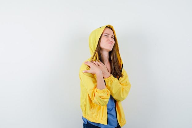 Junge Dame, die unter Schulterschmerzen in T-Shirt, Jacke leidet und müde aussieht, Vorderansicht.