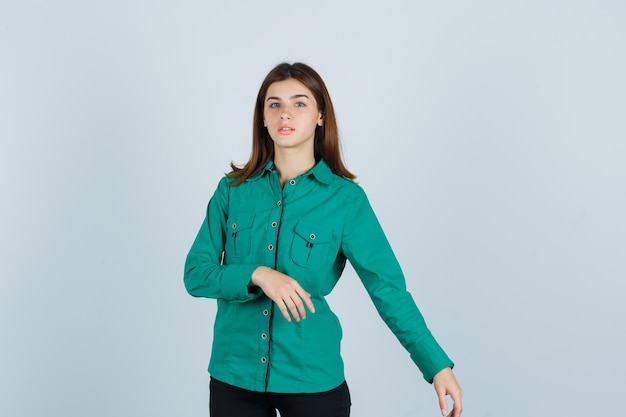 Kostenloses Foto junge dame, die vorgibt, etwas auf ihrer linken seite im grünen hemd zu zeigen und verwirrt aussieht. vorderansicht.