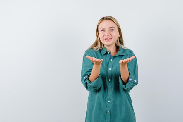 Junge Dame, die vorgibt, etwas in grünem Hemd zu halten oder anzubieten und süß aussieht