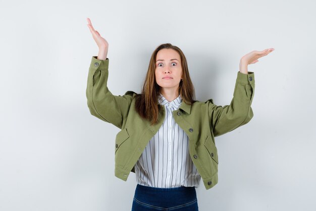 Junge Dame, die vorgibt, etwas in Hemd und Jacke zu präsentieren oder zu erziehen, und sieht verwirrt aus. Vorderansicht.