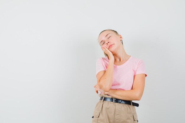 Junge Dame, die Wange auf erhabener Handfläche im T-Shirt und in der Hose lehnt und niedlich aussieht