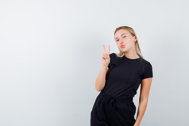 Junge Dame, die Wange auf Finger in T-Shirt, Hose und fröhlich aussehend, Vorderansicht lehnt.