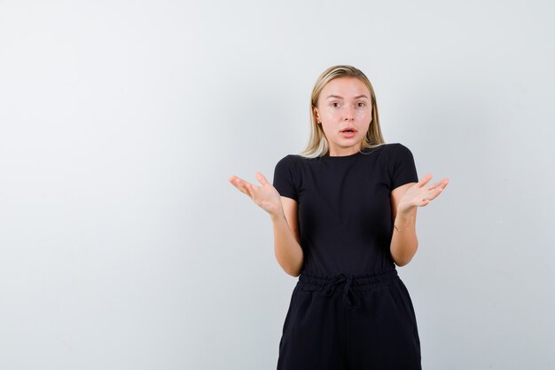 Junge Dame, die Zweifelgeste in T-Shirt, Hose zeigt und ängstlich aussieht. Vorderansicht.