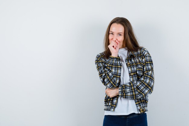 Junge dame drückt faust zum mund in t-shirt, jacke und sieht optimistisch aus. vorderansicht.