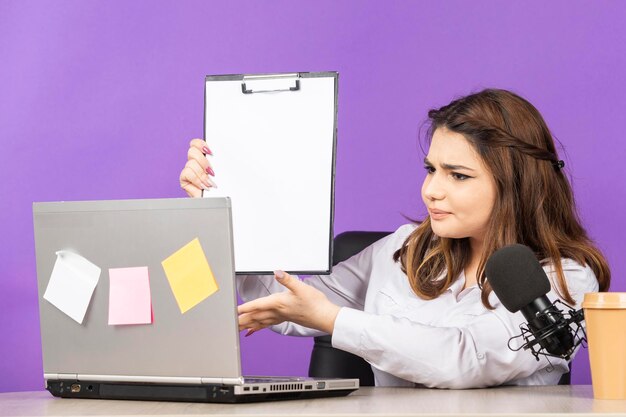 Junge Dame fühlt sich verwirrt und zeigt ihre Notizen an die PC-Kamera Hochwertiges Foto