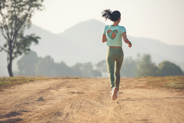 Junge dame genießt einen gesunden lebensstil beim joggen entlang einer landstraße, bewegung und fitness und training im freien. junge dame, die während des sonnenuntergangs auf einer landstraße läuft.