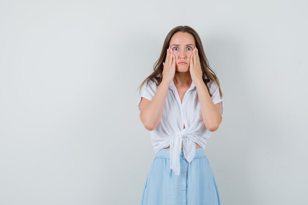 Junge Dame hält Hände auf ihren Wangen in Bluse, Rock und sieht besorgt aus