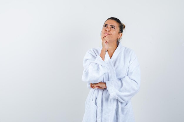 Junge Dame im Bademantel, die in denkender Pose steht und nachdenklich aussieht