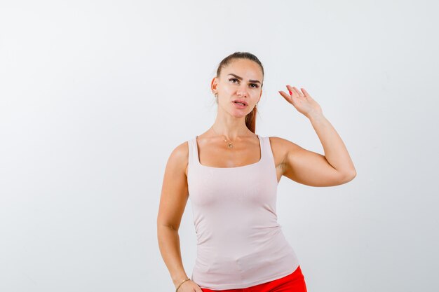 Junge Dame im beigen Trägershirt, das mit erhobener Hand bereitstellt und vorsichtig schaut