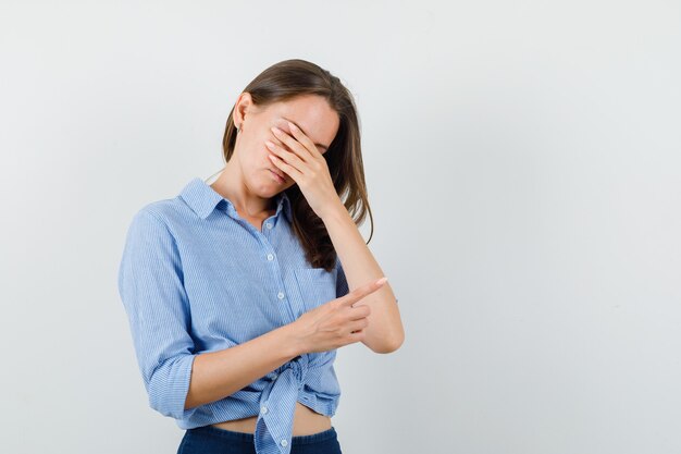 Junge Dame im blauen Hemd, Hose, die Augen bedeckt, während zur Seite zeigt