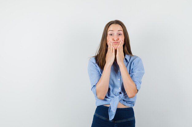 Junge Dame im blauen Hemd, Hosen, die auf wehende Wangen drücken und lustig aussehen