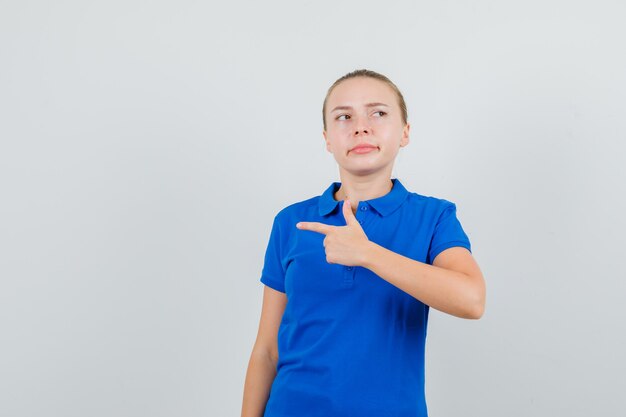 Junge Dame im blauen T-Shirt, das zur Seite zeigt und selbstbewusst aussieht