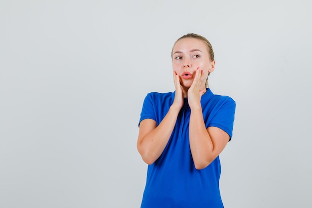 Junge Dame im blauen T-Shirt schaut weg mit den Händen auf der Wange