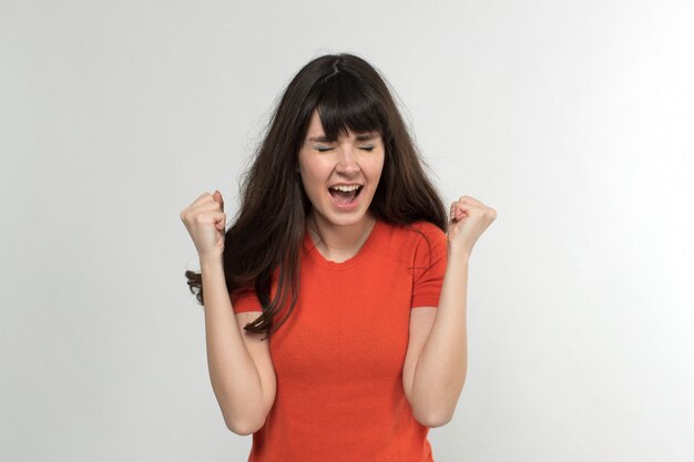 junge Dame im entworfenen T-Shirt, das wütend mit langen Haaren auf Weiß schreit