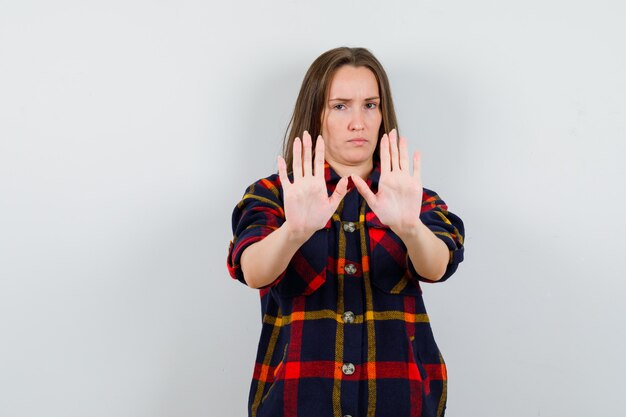 Junge Dame im Freizeithemd, das Stoppgeste zeigt und entschlossen, Vorderansicht schaut.